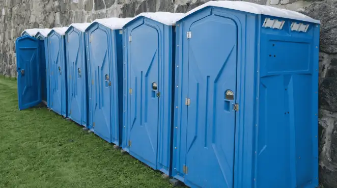 Row of blue portable toilets lined up on grass against a stone wall for event sanitation in Charlotte, NC