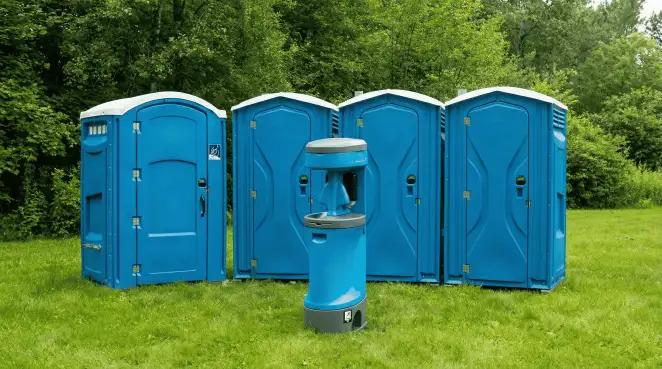 Four blue portable toilets and a matching hand washing station on grass near trees, a common sight at local outdoor events in Charlotte, NC