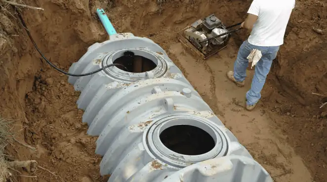 Septic tank installation showing a technician compacting soil around a new poly septic tank in an excavation pit in Charlotte, NC